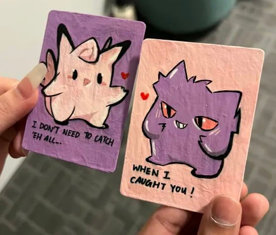 Two small hand-painted cards, held up, with hearts drawn between them